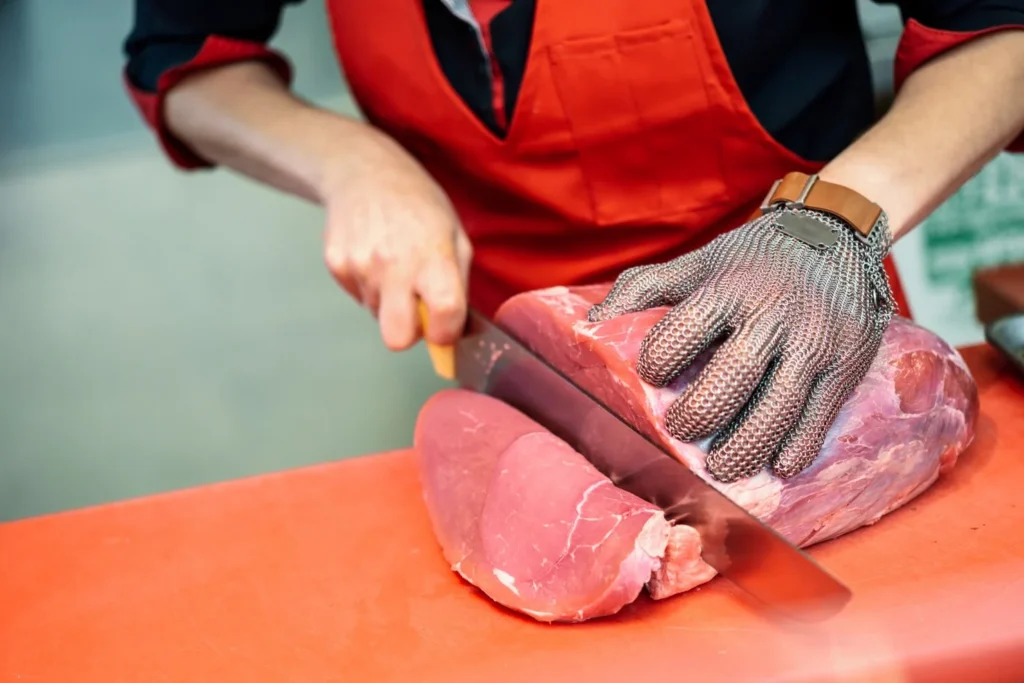 eine-frau-schneidet-frisches-fleisch-in-einem-metzgergeschaeft-mit-einem-metall-sicherheitsnetzhandschuh_1139-1726